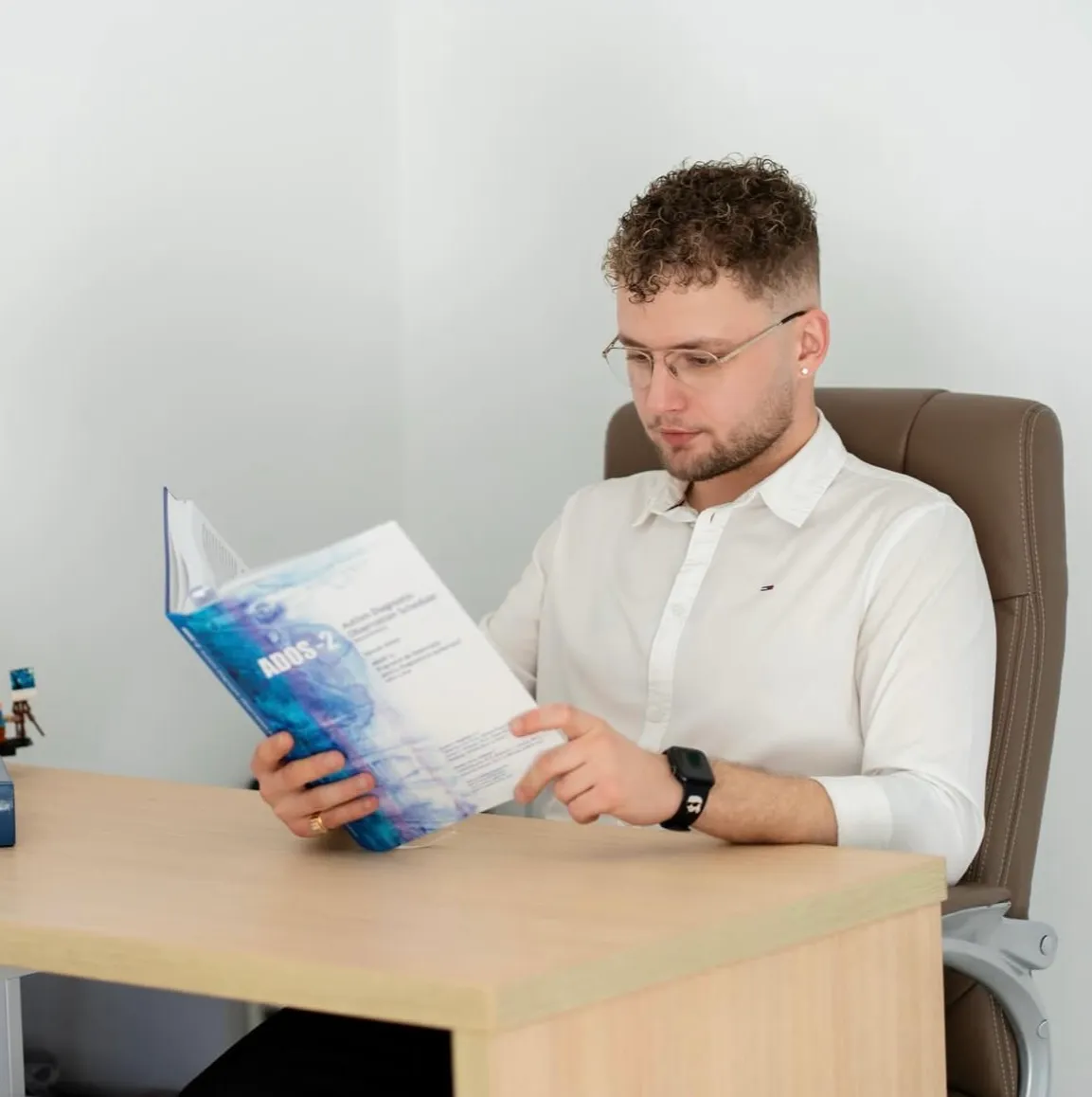 Flaviu Mihăiță studiază un manual de evaluare clinică (ADOS-2), la birou